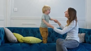 Anne kanepede küçük sarışın çocukla oynayıp eğleniyor.