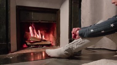 Şirin genç çocuk şöminenin önünde oturmuş, kışın ısınan ateşe bakıyor.