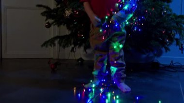 Close-up image of  toddler in a cast illuminated with garland near Christmas tree