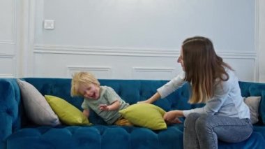 Anne kanepede küçük sarışın çocukla oynayıp eğleniyor.