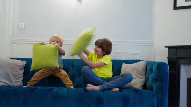 Подушка Бійки Двоє Хлопчиків Розважаються Подушками Сидячи Дивані Вдома Разом — стокове відео