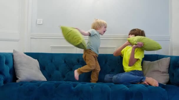 Подушка Бійки Двоє Хлопчиків Розважаються Подушками Сидячи Дивані Вдома Разом — стокове відео
