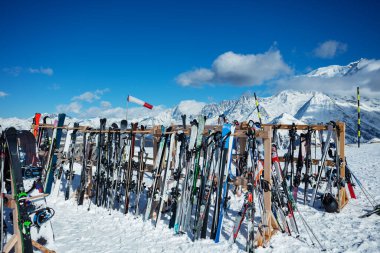Large group skis stand on alpine resort near cafe or restaurant over mountain summits on background