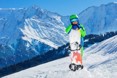 Portrait of a 11 years old happy boy in helmet and ski mask hold snowboard in the mountains