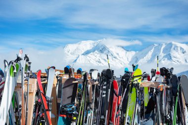 Many skies stand on alpine resort near cafe or restaurant, shop over mountain summits on background