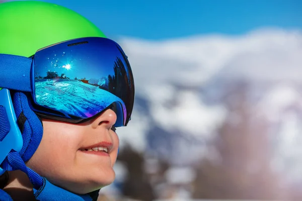 Side portrait of a boy in ski helmet with sport mask glasses over mountains on background