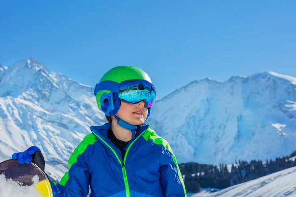 Side portrait of a boy in ski helmet with sport mask glasses over mountains on snowy background