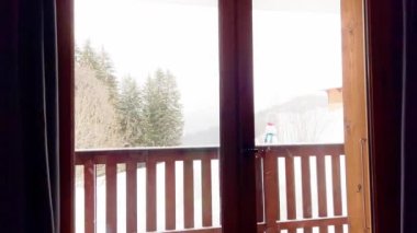 Young boy exit to the balcony in winter sport ski outfit, happily look at snow mountain and forest