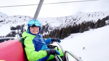 Close portrait of a boy sit in sport outfit with helmet mask and ski going up on chairlift