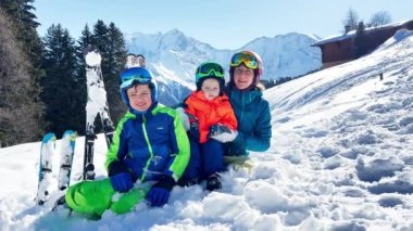 Fun on ski vacations two young boys and mother in sport outfit sit together over mountains on background - family winter vacation