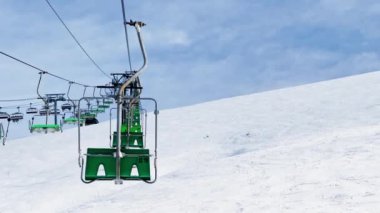 Many ski lift chairs move on rope way at alpine winter resort on sunny day over blue sky