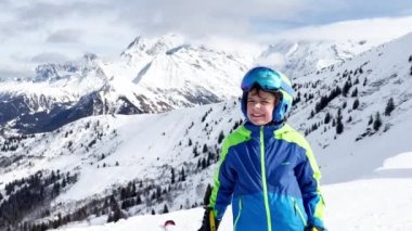 Face portrait of happy boy in ski or snowboard outfit smiling over with mountains peaks on background