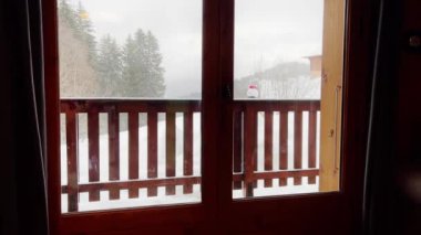 Young boy exit to the balcony in winter sport ski outfit, happily look at snow mountain and forest