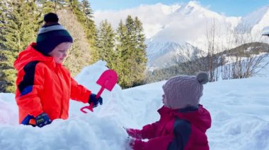 Little boy with sister play  in the snow fortress over mountains on background