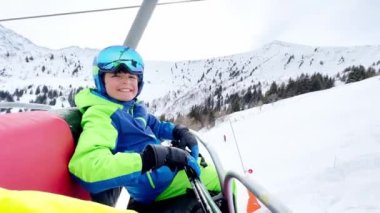 Close portrait of a boy sit in sport outfit with helmet mask and ski going up on chairlift