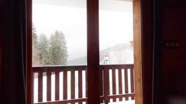 Young boy exit to the balcony in winter sport ski outfit, happily look at snow mountain and forest
