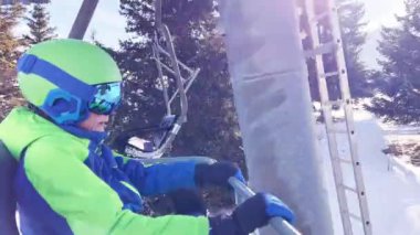 Close portrait of a boy sit in sport outfit with helmet mask and ski going up on chairlift