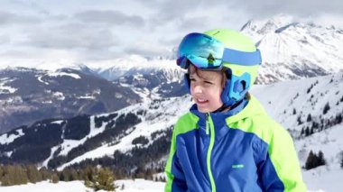 Face portrait of happy boy in ski or snowboard outfit smiling over with mountains peaks on background