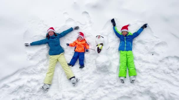 Familie Moeder Zonen Liggen Sneeuw Met Sneeuwpop Santa Hoeden Uitzicht — Stockvideo