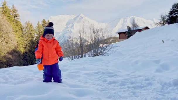 小さな男の子でオレンジコート遊びでシャベルと雪の外で晴れた冬の日 — ストック動画