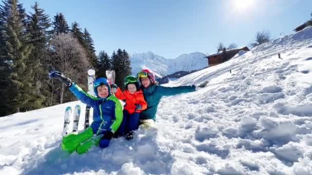 スキー休暇で楽しむ2人の若い男の子とスポーツ衣装の母親が山の上に一緒に座っています 家族の冬の休暇 — ストック動画