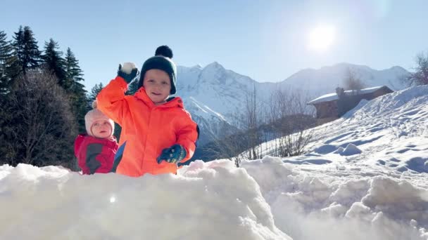 妹を持つ小さな男の子は 背景に山の上の雪の要塞で雪玉をプレイ — ストック動画