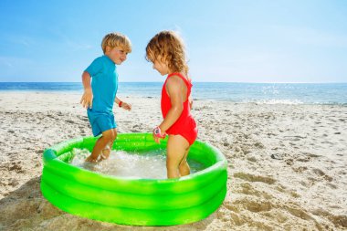 Two happy kids jump splashing in the inflatable pool at the sea beach looking at each other
