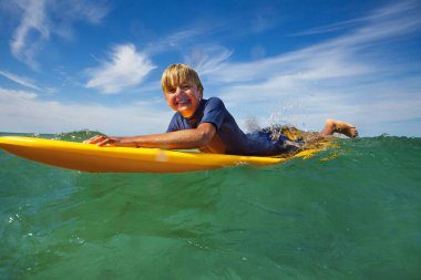 Side portrait of smiling boy lay on the surf board looking at camera in the sea starting to ride the wave
