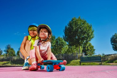 Two children play with skate big brother push little sister skatepark to the ramp slope