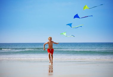 Boy run holding a colorful kite group on the string on the beach smiling over the sky during vacation
