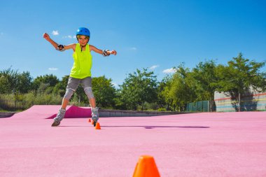 Preteen boy at skate park ride in blue helmet and rollerblades wearing protection going fast around orange cones