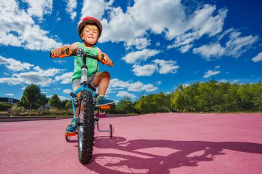 Low angle photo of the cute boy on the little bicycle in a helmet ride in the park over blue sky