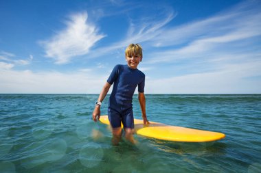 Smiling boy stand with surf board looking at camera in ocean enjoying summer vacations