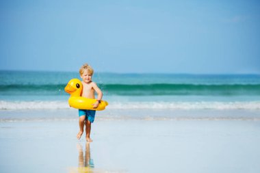 Cute little handsome boy run holding toy inflatable buoys duck having fun running on the sand beach