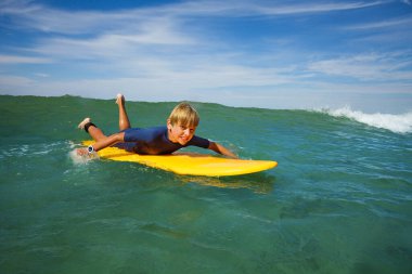 Young boy lay on the surf board and start to paddle to catch the wave learning at surfing school