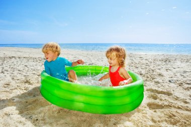 Two happy kids play splashing in the inflatable pool at the sea beach