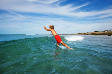 Happy little boy jump running into ocean wave on the summer beach