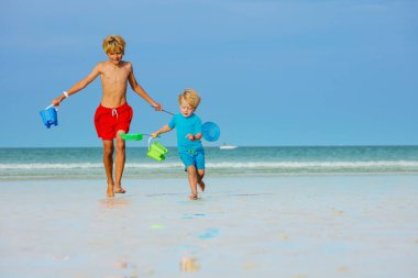 Two boys brothers run on ocean beach holding buckets and hoop-net having fun, play at summer vacations