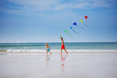 Two children, boys run holding many colorful kite at the beach smiling over the sky during vacation view from profile