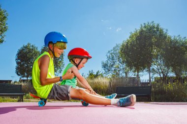 Side view of two brothers sit on the skate at skatepark playing and riding on the ramp