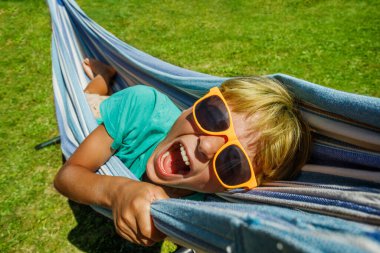 Happy screaming joyful young boy in orange sunglasses lay in hammock close portrait turning head up
