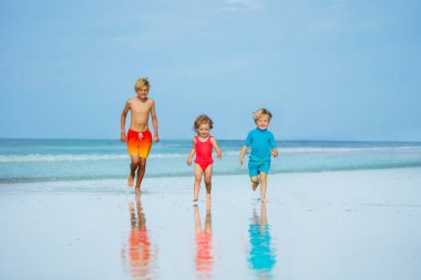 Group of three children boys and girl run together on sand beach wear swimsuits during hot summer day