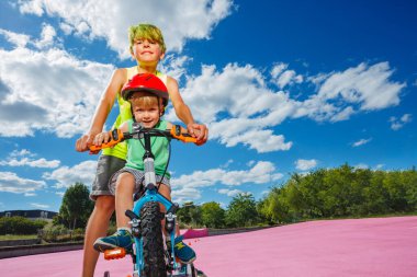 Action close-up image of the big brother helping little boy to push and learn to ride small bicycle in the park
