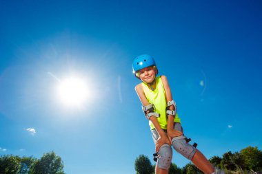 Teen boy in blue helmet skate on rollerblades in the skatepark pose looking down to camera