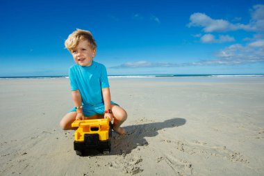 Little Caucasian boy play with and sit on truck toy on the sand sea beach
