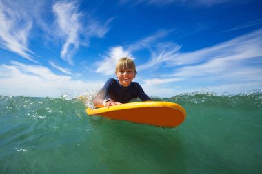 Close face portrait of smiling boy lay on the surf board looking at camera in the sea