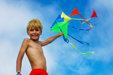 Young smiling boy close portrait stand holding many colorful kites in hand over blue sky