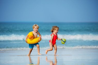 Cute little boy with girl run holding toy inflatable buoys duck and plastic bucket having fun running on the sand beach