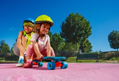 Big brother play with little sister at skatepark wearing helmet pushing her on the ramp