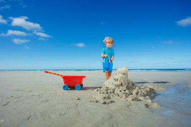 Happy smiling boy play with sand and water at the ocean beach during summer vacations